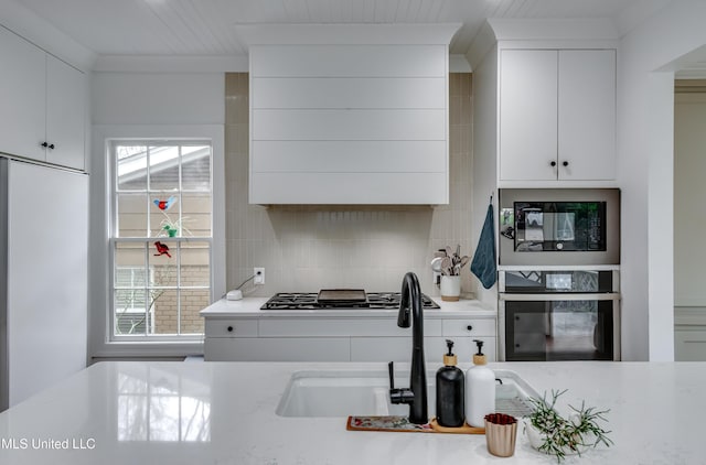 kitchen with sink, crown molding, built in appliances, tasteful backsplash, and white cabinets