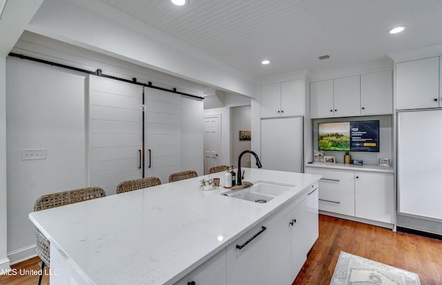 kitchen with white cabinetry, sink, paneled built in refrigerator, a barn door, and a center island with sink