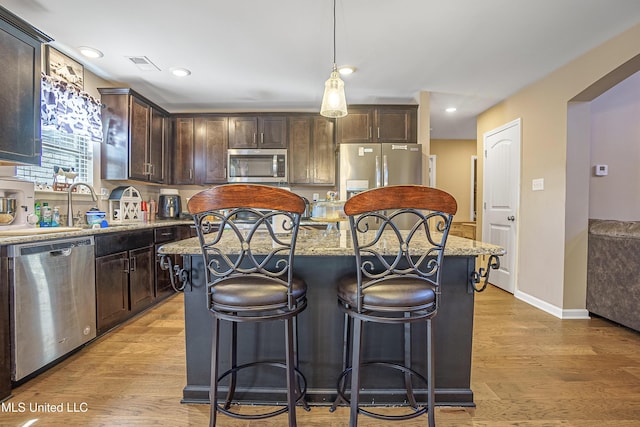 kitchen featuring dark brown cabinetry, appliances with stainless steel finishes, decorative light fixtures, and a center island