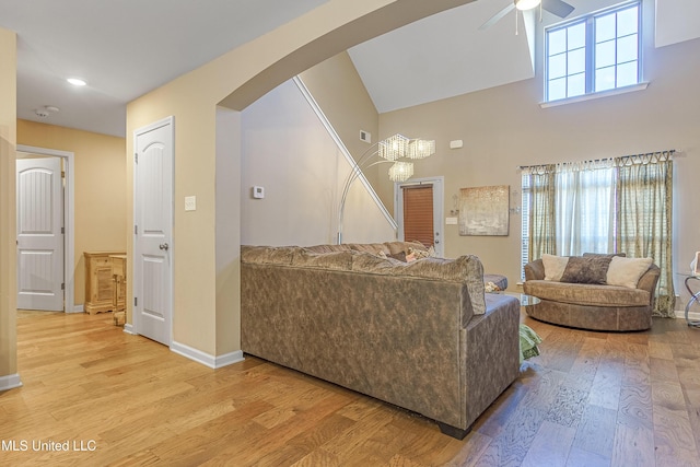 living room with ceiling fan, a high ceiling, and light wood-type flooring