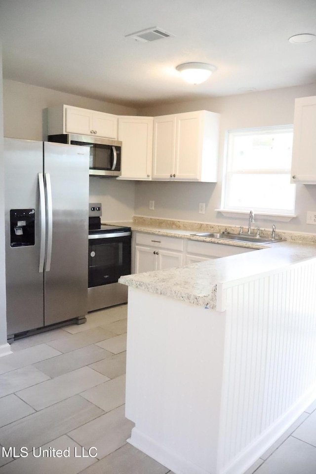 kitchen featuring white cabinets, a peninsula, stainless steel appliances, and a sink