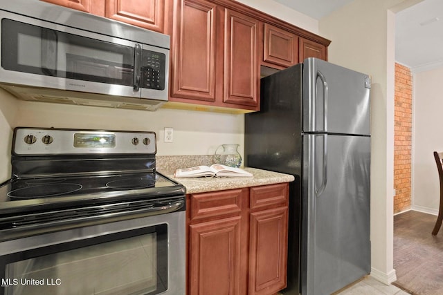 kitchen featuring crown molding, appliances with stainless steel finishes, light stone counters, and light hardwood / wood-style floors