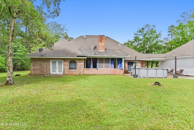 rear view of house with brick siding, an outdoor pool, french doors, a yard, and roof with shingles