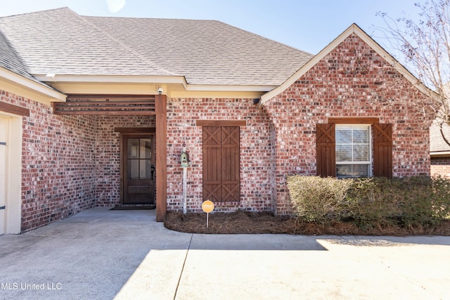 doorway to property with a shingled roof and brick siding