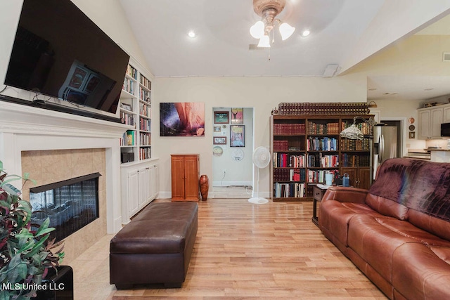 living room with lofted ceiling, light hardwood / wood-style flooring, built in shelves, a fireplace, and ceiling fan