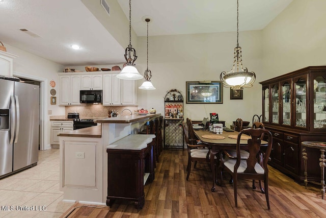 kitchen with hanging light fixtures, backsplash, white cabinetry, light wood-type flooring, and black appliances