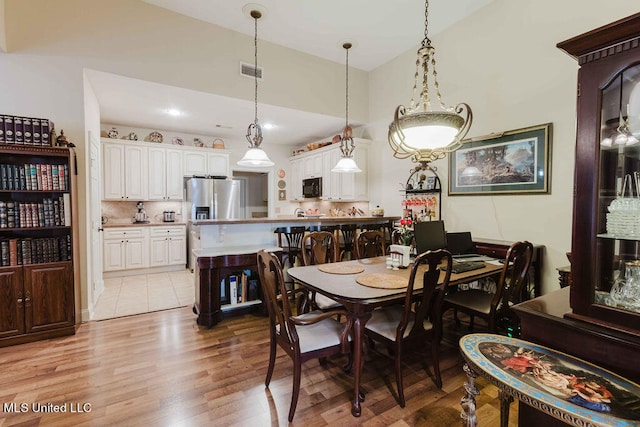 dining room with high vaulted ceiling and light wood-type flooring