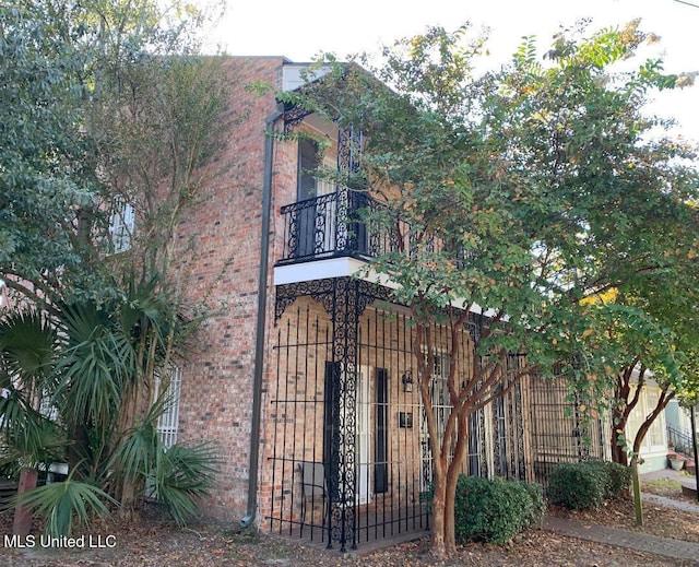 view of home's exterior featuring brick siding, fence, a gate, and a balcony