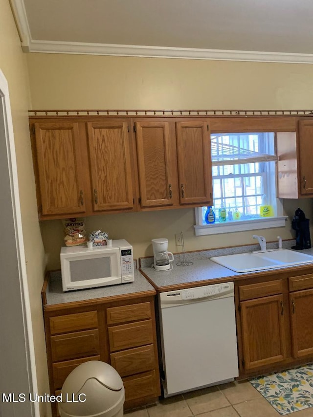 kitchen with a sink, light tile patterned flooring, brown cabinetry, white appliances, and ornamental molding