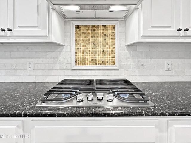 kitchen view of range hood, stainless steel gas cooktop, white cabinets, and decorative backsplash