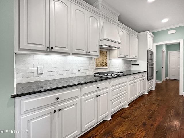 kitchen featuring custom range hood, stainless steel appliances, white cabinetry, dark stone counters, and backsplash