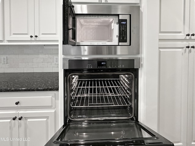 kitchen view of stainless steel microwave, white cabinets, backsplash, and dark stone countertops