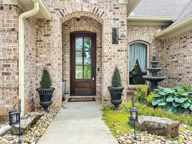 view of exterior entry with brick siding and roof with shingles