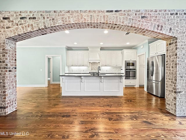kitchen featuring stainless steel appliances, ornamental molding, dark countertops, dark wood-type flooring, and white cabinets