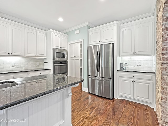 kitchen featuring appliances with stainless steel finishes, dark stone countertops, dark wood-style floors, white cabinetry, and ornamental molding