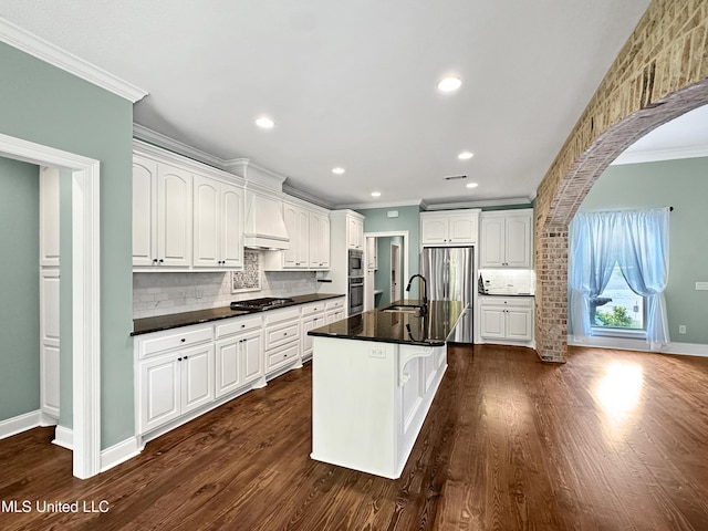 kitchen with ornamental molding, appliances with stainless steel finishes, arched walkways, backsplash, and dark countertops