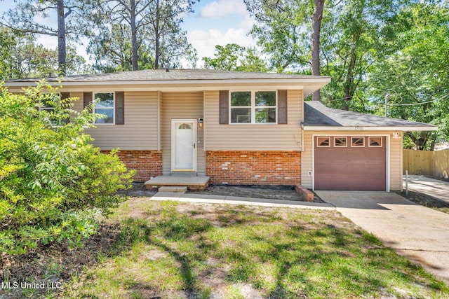 raised ranch featuring driveway, roof with shingles, brick siding, fence, and an attached garage