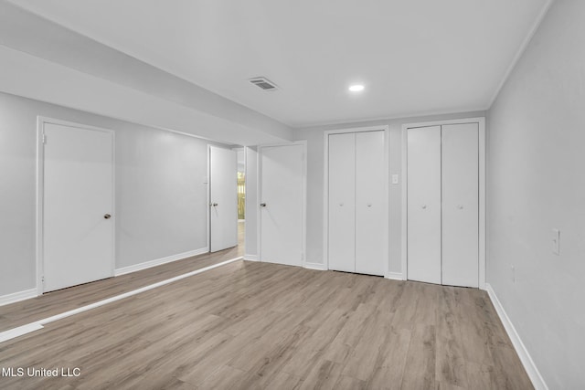 unfurnished bedroom with visible vents, baseboards, multiple closets, and wood finished floors