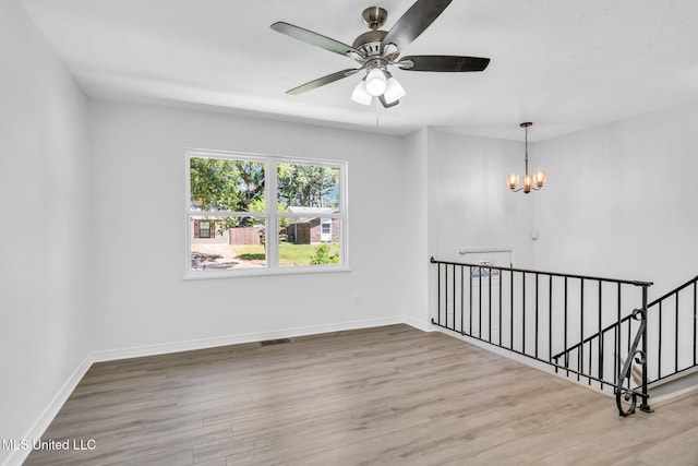 unfurnished room with baseboards, ceiling fan with notable chandelier, wood finished floors, and visible vents