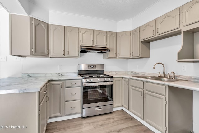 kitchen featuring stainless steel range with gas stovetop, a sink, light countertops, light wood-style floors, and under cabinet range hood