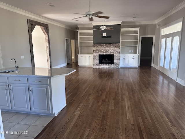 unfurnished living room with ornamental molding, a ceiling fan, a sink, a fireplace, and dark wood-style flooring