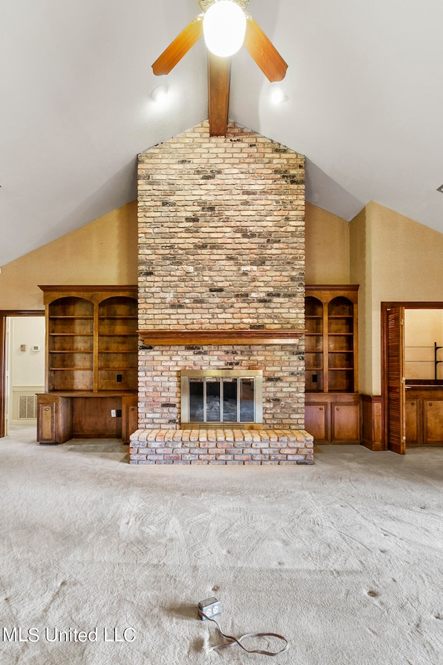 unfurnished living room with a brick fireplace, ceiling fan, beamed ceiling, carpet, and built in shelves