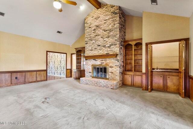 unfurnished living room featuring beam ceiling, light carpet, a brick fireplace, built in features, and wood walls