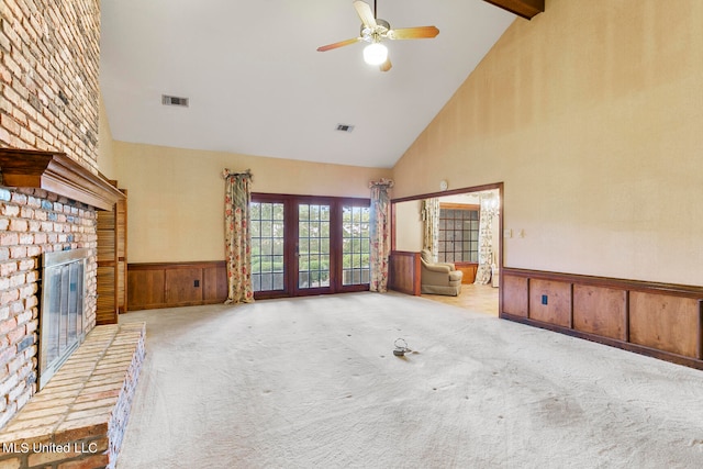 unfurnished living room featuring beam ceiling, light colored carpet, a fireplace, high vaulted ceiling, and wood walls