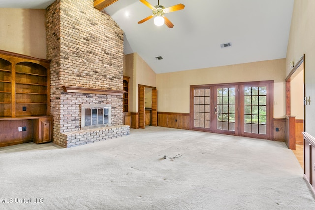 unfurnished living room featuring wood walls, a brick fireplace, ceiling fan, light carpet, and high vaulted ceiling