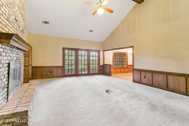 unfurnished living room featuring ceiling fan, high vaulted ceiling, a fireplace, wooden walls, and light colored carpet