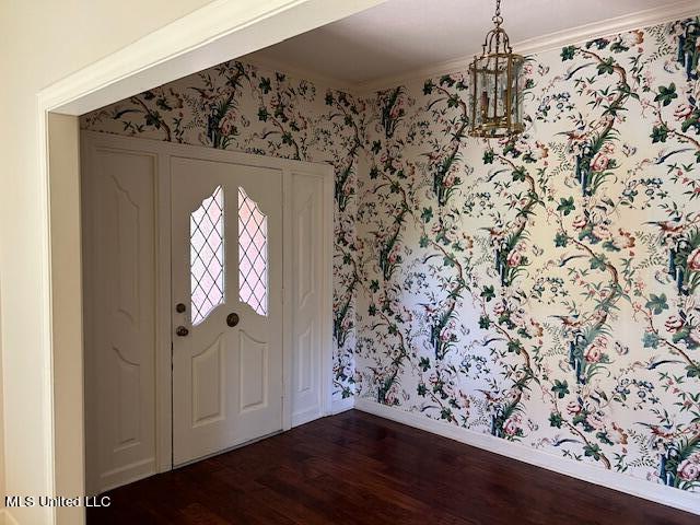 entrance foyer featuring dark wood-type flooring, crown molding, and a notable chandelier