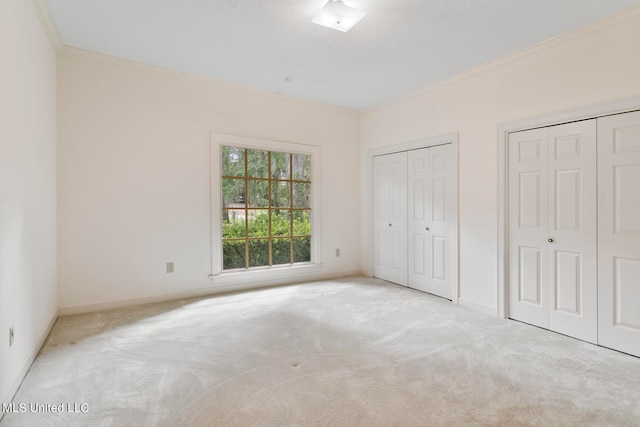 unfurnished bedroom with crown molding, two closets, and light colored carpet