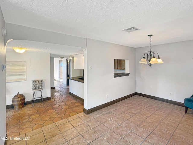 spare room with a chandelier, a textured ceiling, and tile patterned flooring