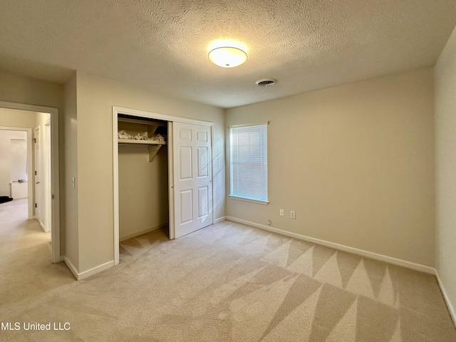 unfurnished bedroom with a textured ceiling, a closet, and light carpet