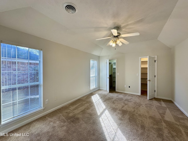 unfurnished bedroom with ceiling fan, vaulted ceiling, light carpet, a walk in closet, and a closet