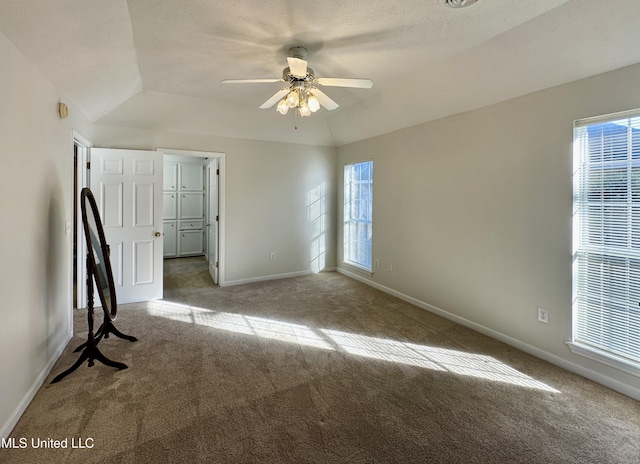 empty room featuring ceiling fan, plenty of natural light, carpet flooring, and vaulted ceiling