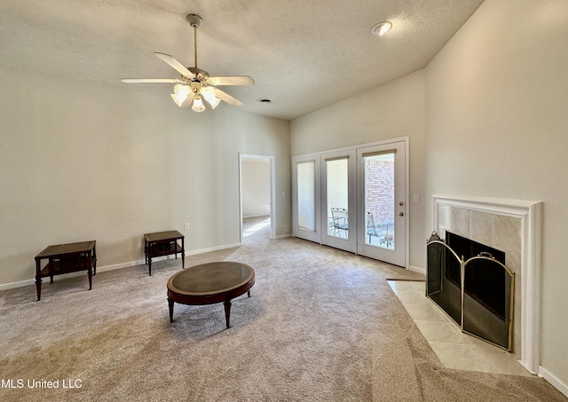 living area featuring ceiling fan, light colored carpet, a tile fireplace, and a textured ceiling