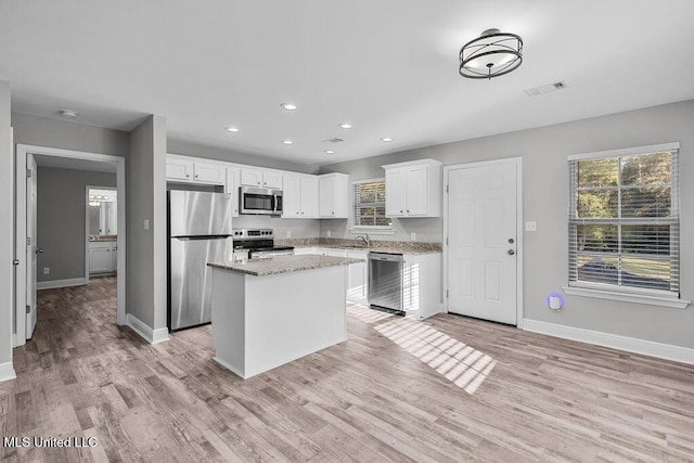 kitchen featuring a center island, light hardwood / wood-style flooring, light stone countertops, white cabinetry, and stainless steel appliances