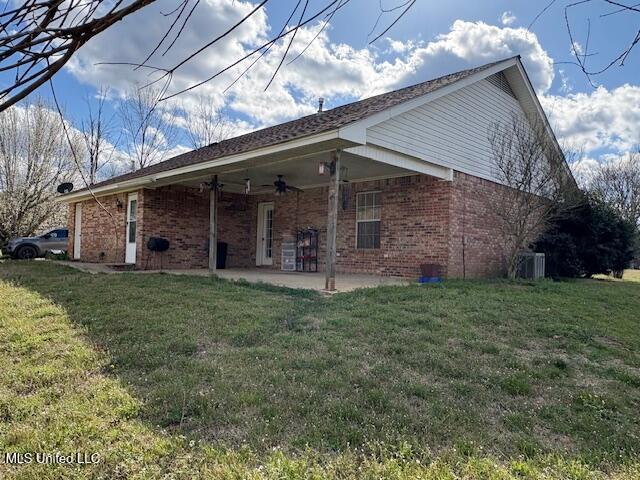 back of property with a yard, a ceiling fan, and brick siding