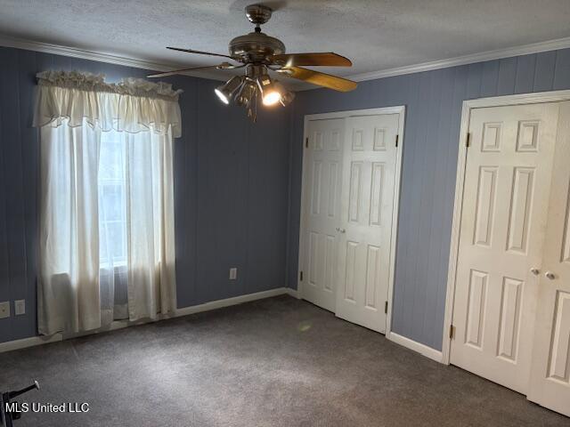 unfurnished bedroom featuring a ceiling fan, carpet, baseboards, a textured ceiling, and crown molding