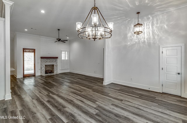 unfurnished living room featuring ceiling fan with notable chandelier, a brick fireplace, ornamental molding, and dark wood-type flooring