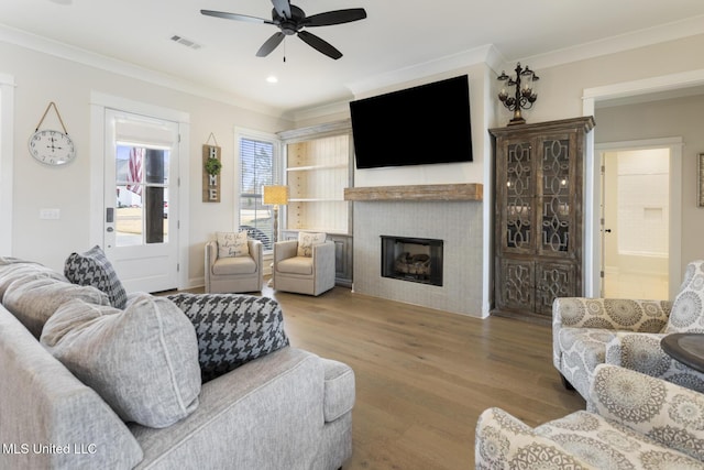 living room with ceiling fan, a fireplace, wood-type flooring, and ornamental molding