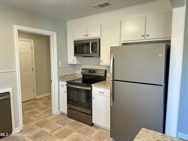 kitchen featuring light stone countertops, white cabinetry, a textured ceiling, and appliances with stainless steel finishes