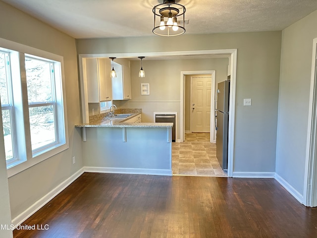 kitchen featuring hanging light fixtures, kitchen peninsula, stainless steel fridge, a breakfast bar area, and white cabinets