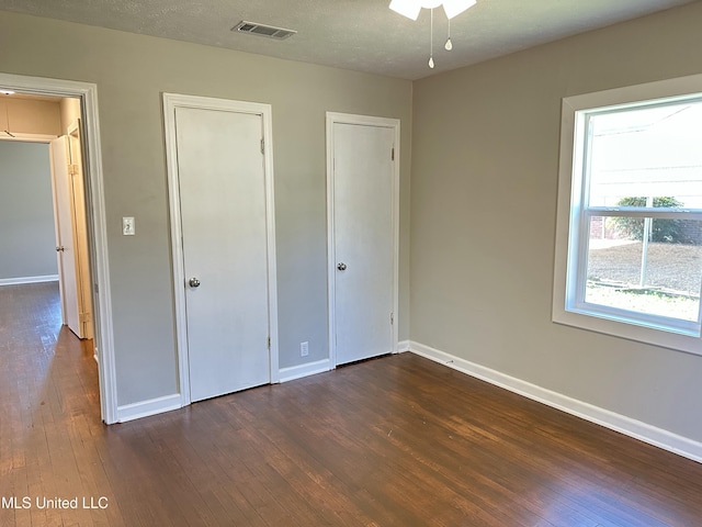 unfurnished bedroom featuring a textured ceiling, dark hardwood / wood-style floors, and multiple closets