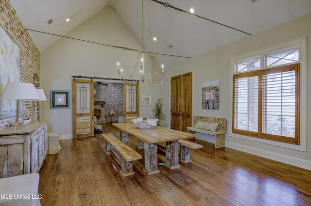 dining space featuring hardwood / wood-style flooring, a barn door, a notable chandelier, and high vaulted ceiling