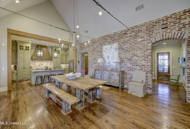 dining room with hardwood / wood-style flooring, brick wall, and high vaulted ceiling