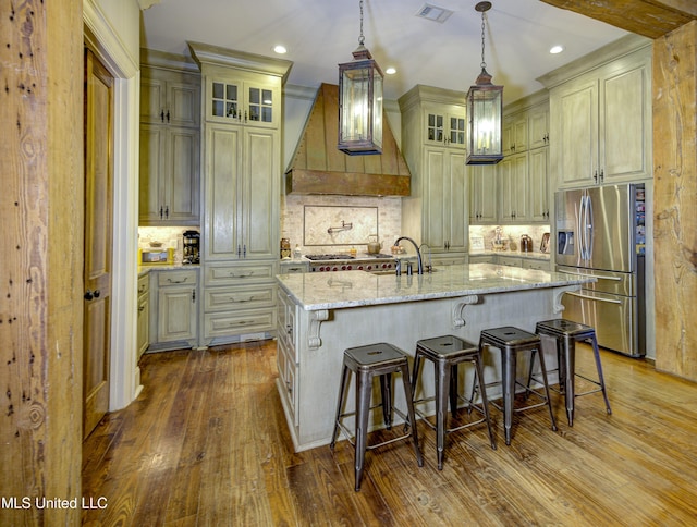 kitchen with backsplash, hanging light fixtures, light stone counters, an island with sink, and stainless steel fridge with ice dispenser