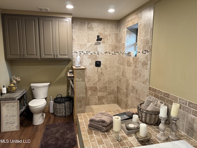 bathroom featuring wood-type flooring, toilet, and a tile shower