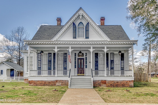 view of front facade with a chimney, roof with shingles, fence, a porch, and a front yard